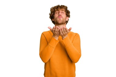 Genç beyaz adam yeşil renkli arka planda izole edilmiş dudaklar kıvrılıyor ve hava öpücüğü göndermek için avuç içleri tutuyor..