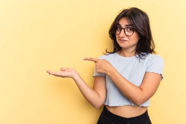 Sarı arka planda izole edilmiş genç Hintli bir kadın, elinde bir fotokopi odası tutarken heyecanlı..