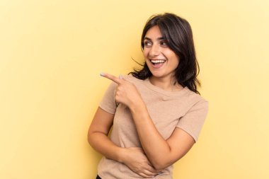 Sarı arka planda izole edilmiş genç Hintli kadın gülümseyen, neşeli ve keyifli bir kenara bakıyor..