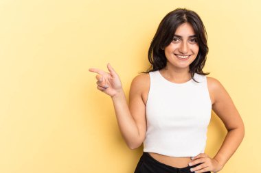 Sarı arka planda izole edilmiş genç Hintli kadın işaret parmağıyla işaret ederek gülümsüyor..