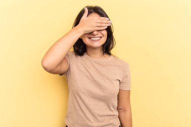 Sarı arka planda izole edilmiş genç bir Hintli kadın elleriyle gözlerini kapatıyor, geniş bir gülümsemeyle bir sürpriz bekliyor..