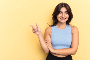 Sarı arka planda izole edilmiş genç Hintli kadın işaret parmağıyla işaret ederek gülümsüyor..