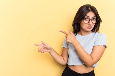 Sarı arka planda izole edilmiş genç bir Hintli kadın işaret parmağıyla fotokopi alanını işaret ederek heyecan ve arzusunu ifade ediyor..