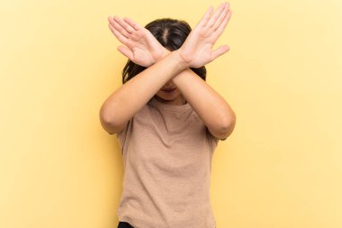 Sarı arka planda izole edilmiş genç Hintli kadın iki kolu çapraz tutuyor, inkar kavramı.