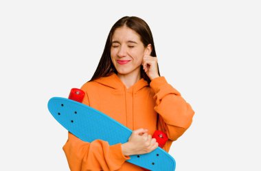 Genç kaykaycı beyaz kadın kulaklarını elleriyle kapatıyor..