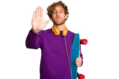 Young skater caucasian man isolated on white background standing with outstretched hand showing stop sign, preventing you.
