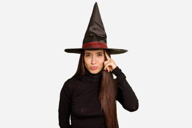 Cadılar bayramı için cadı gibi giyinmiş genç beyaz bir kadın tapınağı parmağıyla göstererek, düşünerek, bir göreve odaklanmış..