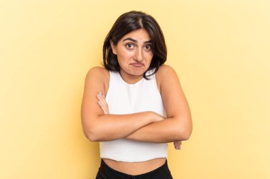 Sarı arka planda izole edilmiş genç Hintli kadın omuzlarını silker ve gözleri açık kalır..