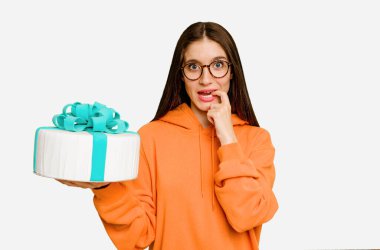 Elinde doğum günü pastası tutan genç beyaz kadın tırnak yiyor, gergin ve çok endişeli..