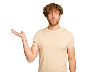 Yeşil krom arka planda izole edilmiş genç beyaz adam, avuç içi fotokopi alanını tutmaktan etkilenmiş..