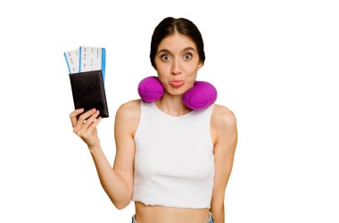 Pasaportunda şişirilebilir seyahat yastığı olan genç beyaz kadın omuz silkiyor ve gözleri açık..