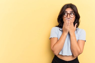 Genç Hintli bir kadın sarı arka planda izole edilmiş. Düşünceli bir şekilde bir fotokopi odasına bakıyor. Ağzını eliyle kapatıyor..