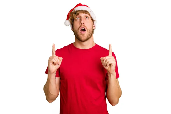 若いですCaucasian男身に着けていますAクリスマスサンタ帽子隔離された上に白い背景ポインティング上向きにオープン口 — ストック写真