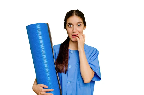 Young Caucasian Physiotherapist Woman Holding Mat Isolated Biting Fingernails Nervous — Stock Photo, Image
