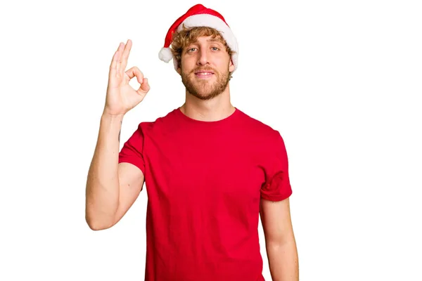 若いですCaucasian男身に着けていますAクリスマスサンタ帽子隔離上の白い背景陽気で自信を持ってショーOkジェスチャー — ストック写真