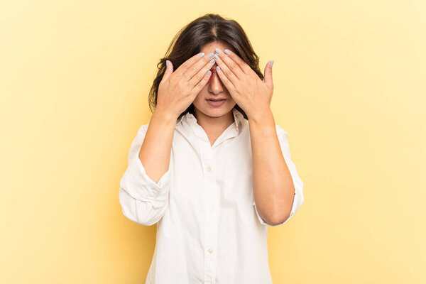 Young Indian woman isolated on yellow background afraid covering eyes with hands.