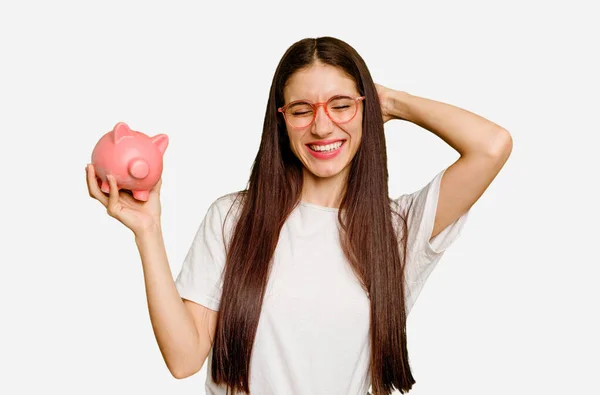 Young Caucasian Woman Holding Piggy Bank Isolated Touching Back Head — Stock Photo, Image