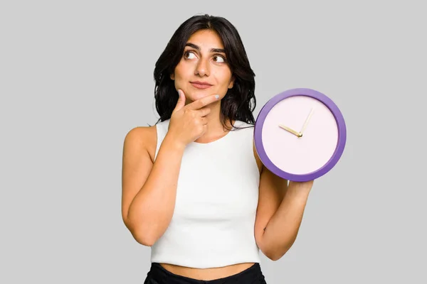 Young Indian Woman Holding Clock Isolated Looking Sideways Doubtful Skeptical — Stock Photo, Image