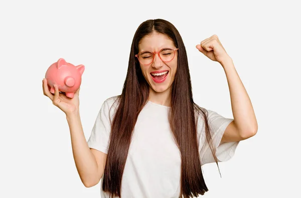 Young Caucasian Woman Holding Piggy Bank Isolated Raising Fist Victory — Stock Photo, Image