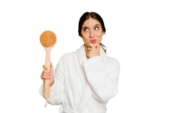 Young Caucasian Woman Holding Shower Brush Isolated Looking Sideways Doubtful — Stock Photo, Image