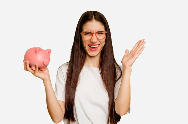 Young Caucasian Woman Holding Piggy Bank Isolated Receiving Pleasant Surprise — Stock Photo, Image