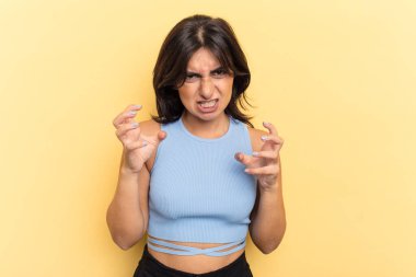 Sarı arka planda izole edilmiş genç Hintli kadın gergin elleriyle çığlık atıyor..