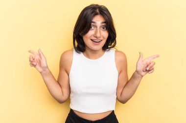 Sarı arka planda izole edilmiş genç Hintli kadın farklı kopya alanlarını gösteriyor, birini seçiyor, parmaklarıyla gösteriyor..