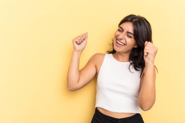 Genç Hintli kadın sarı arka planda izole edilmiş zafer sonrası yumruğunu kaldırıyor, kazanan konsept..