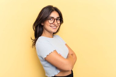 Sarı arka planda izole edilmiş genç Hintli kadın mutlu, güler yüzlü ve neşeli.