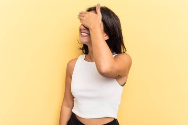 Sarı arka planda izole edilmiş genç bir Hintli kadın elleriyle gözlerini kapatıyor, geniş bir gülümsemeyle bir sürpriz bekliyor..