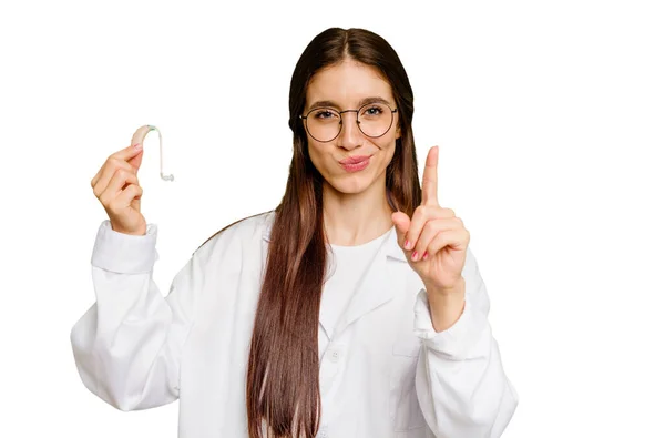 Mujer Joven Otorrinolaringóloga Caucásica Sosteniendo Audífono Aislado Mostrando Número Uno — Foto de Stock