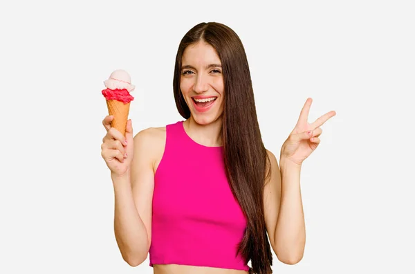 年轻的高加索女人吃着冰淇淋 孤立地快乐而无忧无虑 用手指展示和平的象征 — 图库照片