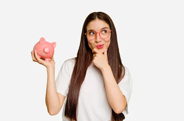 Young Caucasian Woman Holding Piggy Bank Isolated Looking Sideways Doubtful — Stock Photo, Image