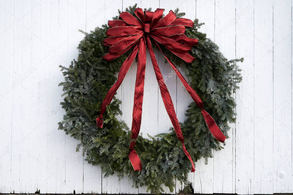 Natural evergreen holiday wreath with red ribbons on old rustic wood siding with peeling paint