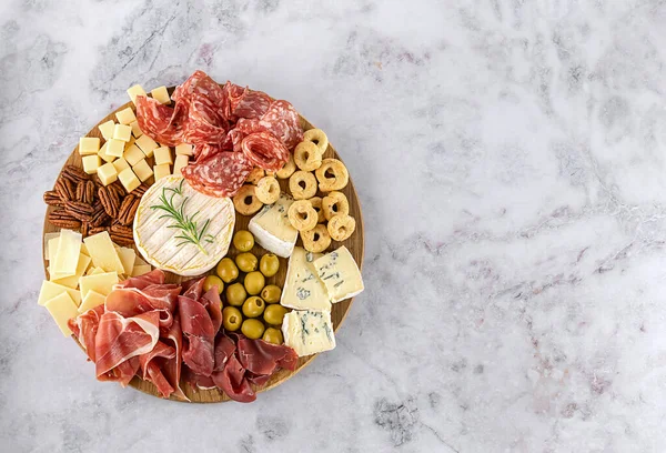 Vista superior de la sabrosa tabla de embutidos con queso, uva, nueces, aceitunas y jamón en un plato de cocina circular — Foto de Stock
