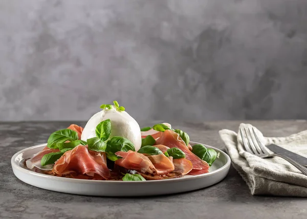 Bufalo burrata peyniri taze domates, jambon ve fesleğen yapraklarıyla servis edilir.. 