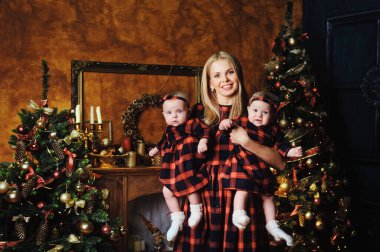 Mutlu bir anne ve ikiz çocukları Noel ağacının arka planında, evin içinde..