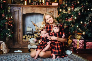 Mutlu bir anne ve ikiz çocukları Noel ağacının arka planında, evin içinde..