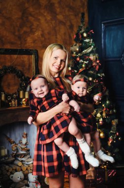 Mutlu bir anne ve ikiz çocukları Noel ağacının arka planında, evin içinde..