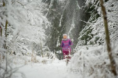 Kışın mor elbiseli küçük bir kız karla kaplı bir ormanda yürüyor.