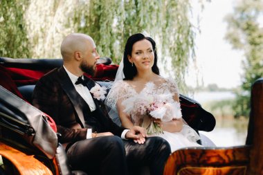 Gelin ve damat bir buketle doğada eski tarzda bir arabada oturuyorlar..