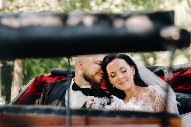 Gelin ve damat bir buketle doğada eski tarzda bir arabada oturuyorlar..