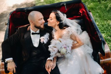 Gelin ve damat bir buketle doğada eski tarzda bir arabada oturuyorlar..