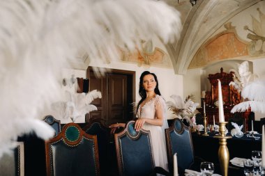 Masalarda tüylerle süslenmiş bir restoranın içinde gelinlik giymiş şık bir gelin..