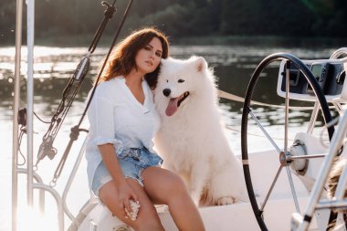 Denizde beyaz bir yatta büyük beyaz bir köpeği olan mutlu bir kadın..