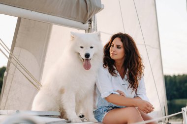 Denizde beyaz bir yatta büyük beyaz bir köpeği olan mutlu bir kadın..