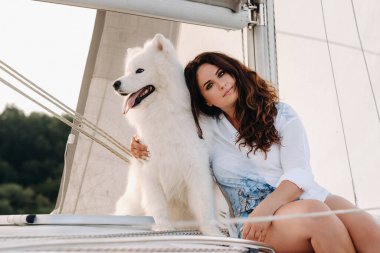 Denizde beyaz bir yatta büyük beyaz bir köpeği olan mutlu bir kadın..