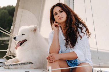 Denizde beyaz bir yatta büyük beyaz bir köpeği olan mutlu bir kadın..