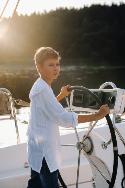 Yatta dümende küçük bir kaptan. Gün batımında yatta kaptanın dümeninde küçük bir çocuk..