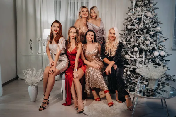 Mujeres sexy en vestidos están sentados en el sofá cerca del árbol de Navidad en el interior de la casa —  Fotos de Stock